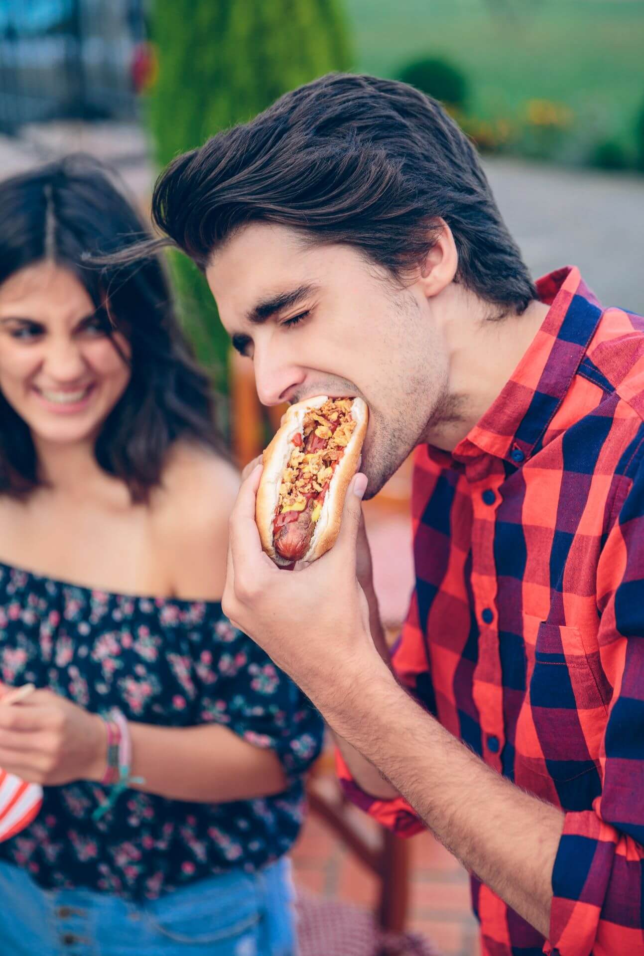 young-man-eating-hot-dog-and-woman-laughing-in-bac-2025-03-13-02-27-01-utc